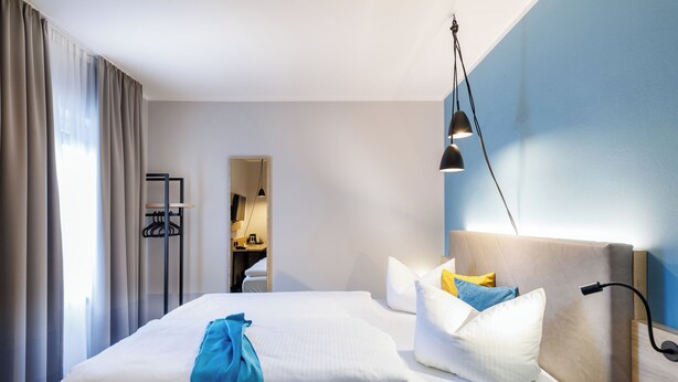 A hotel room with a bed, a bedside table, a lamp, and a view of the hallway. - Hotel Purucker (Kulmbach)