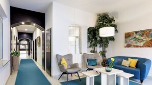 A modern living room with a blue sofa, two armchairs, a coffee table, and a hallway leading to a kitchen. - Hotel Purucker (Kulmbach)
