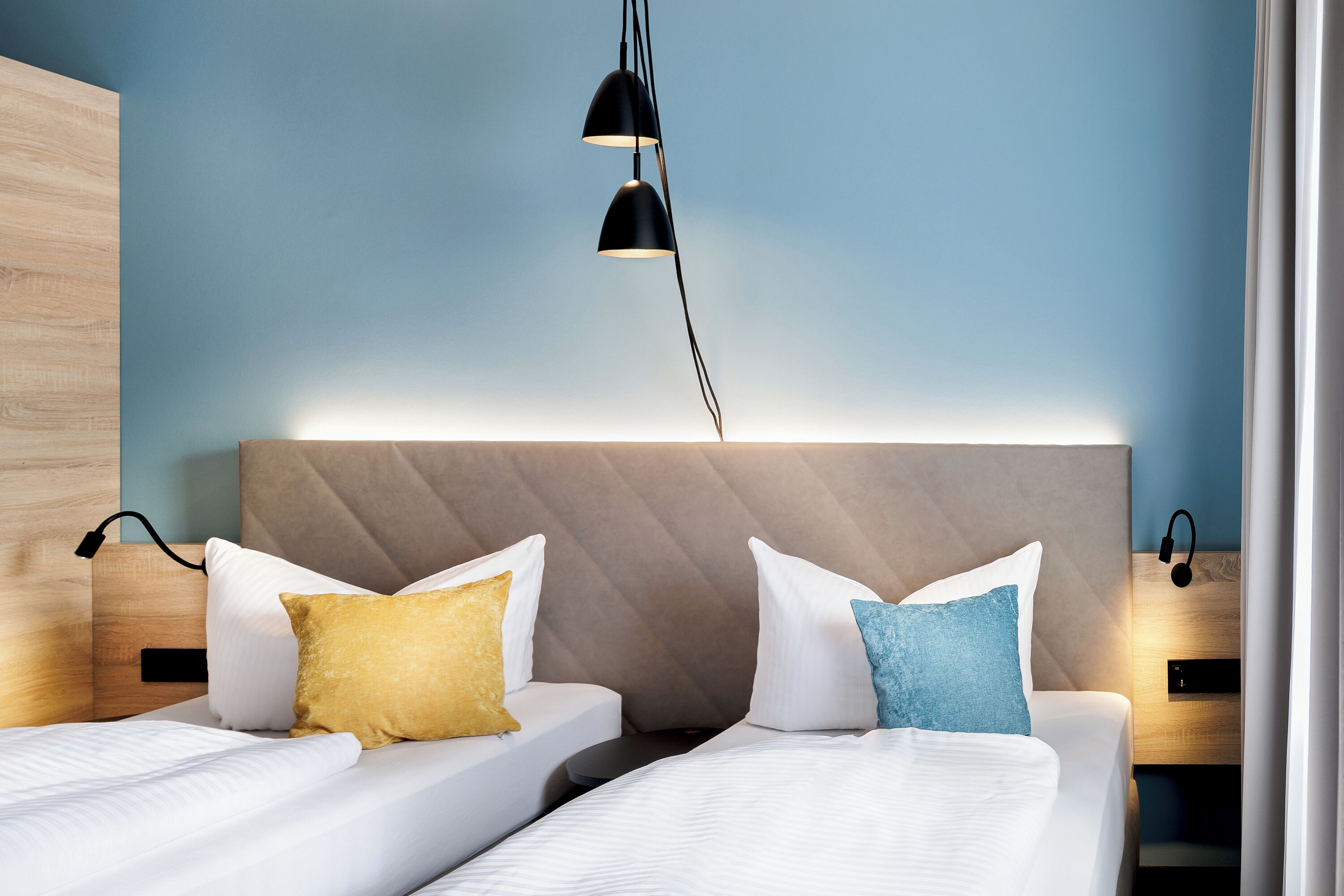 A hotel room with two beds, a wooden headboard, and a modern pendant light.