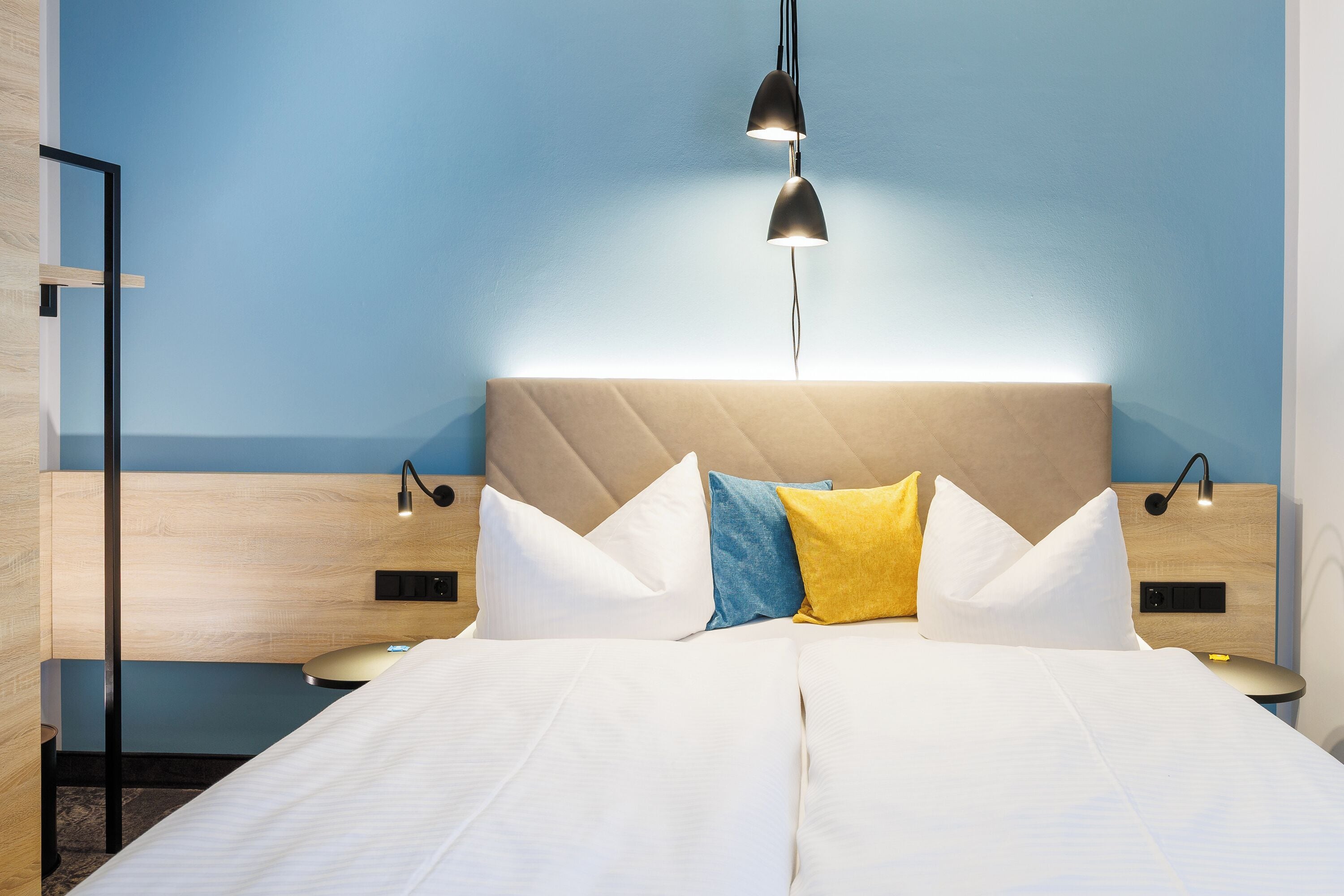 A modern hotel room with a large bed, a headboard with built-in lighting, bedside tables with lamps, and a view of the sea.