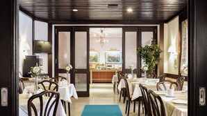 A hotel dining area with tables set for guests, a bar in the background, and a large plant in the center. - Hotel Purucker (Kulmbach)