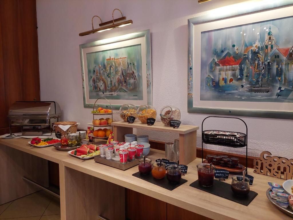 Un bufé de desayuno con diversas opciones de comida y bebidas, obras de arte enmarcadas en las paredes y una máquina de café.
