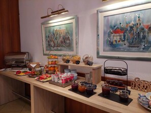 Un bufé de desayuno con diversas opciones de comida y bebidas, obras de arte enmarcadas en las paredes y una máquina de café.