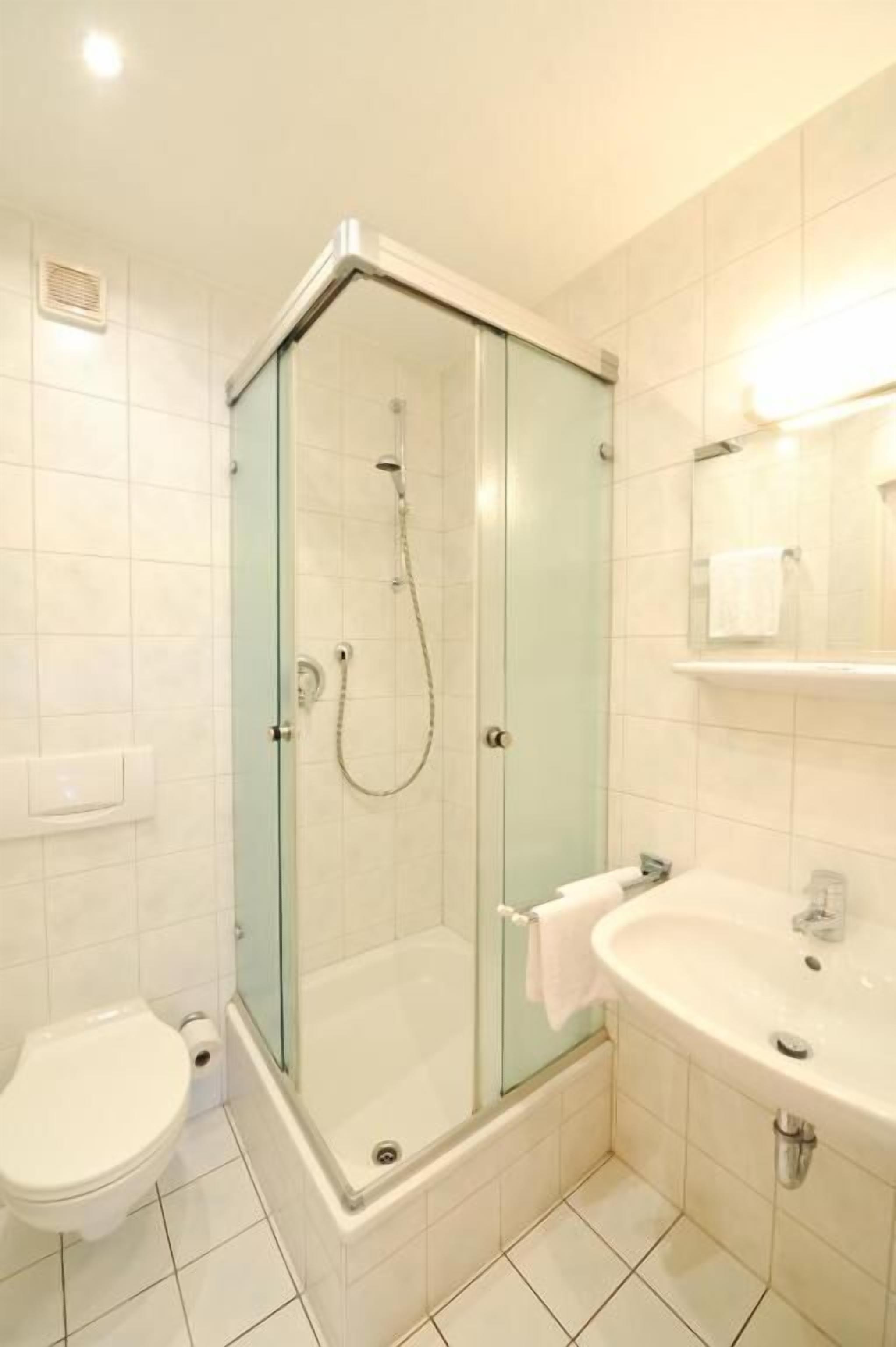 Un baño con ducha de vidrio, inodoro y lavamanos con espejo.