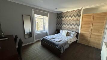 A bedroom with a bed, a desk, a chair, a window, and a wardrobe.