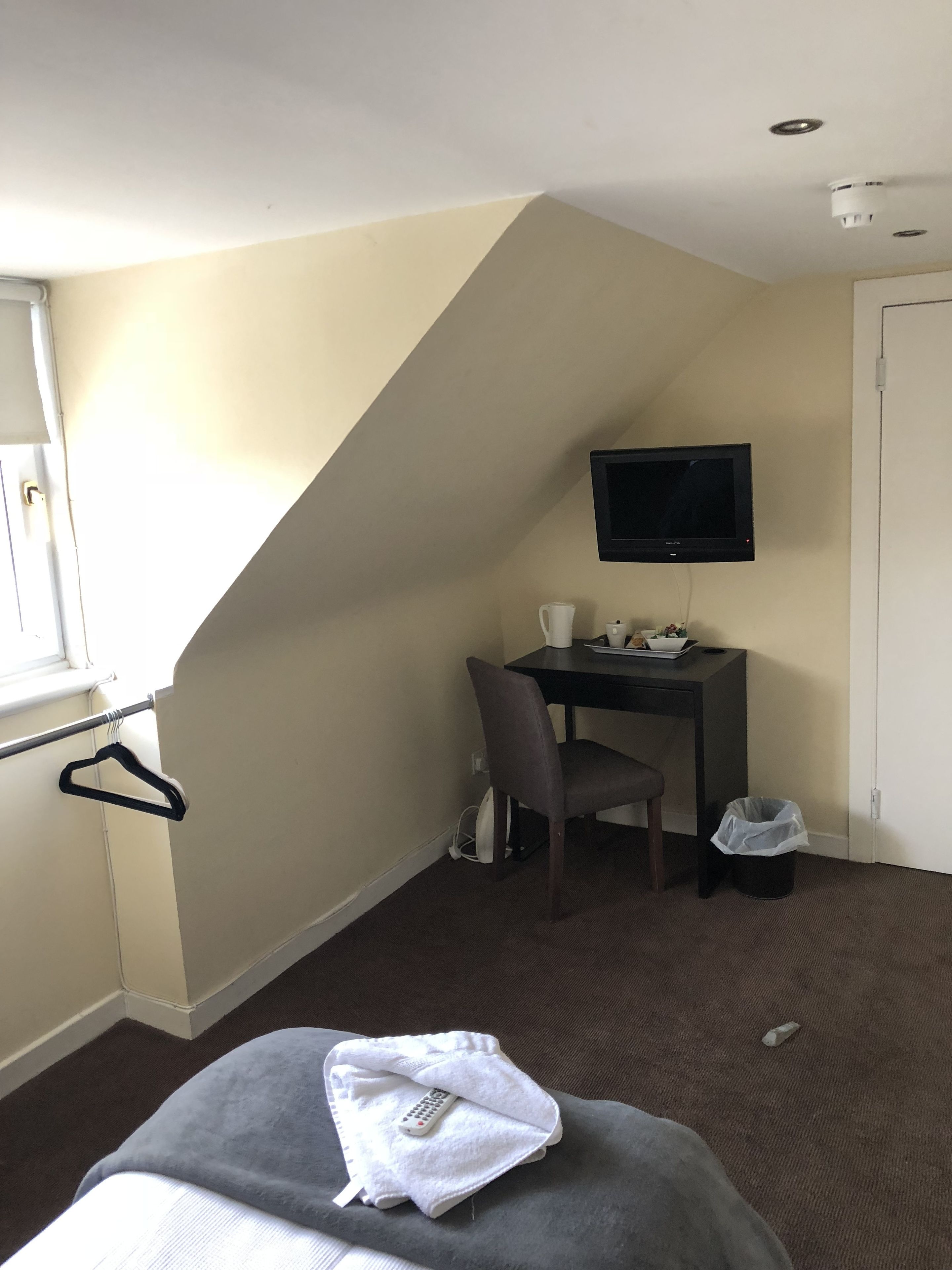 A hotel room with a bed, a desk, a chair, a television, and a window.