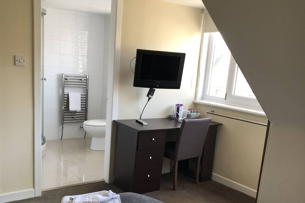 A bedroom with a bed, a desk, a television, and a bathroom visible through an open door.