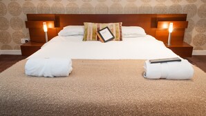A neatly made bed with a pillow, two bedside lamps, and two rolled towels on a textured carpet. - Rooms at 31 (Stonehaven)