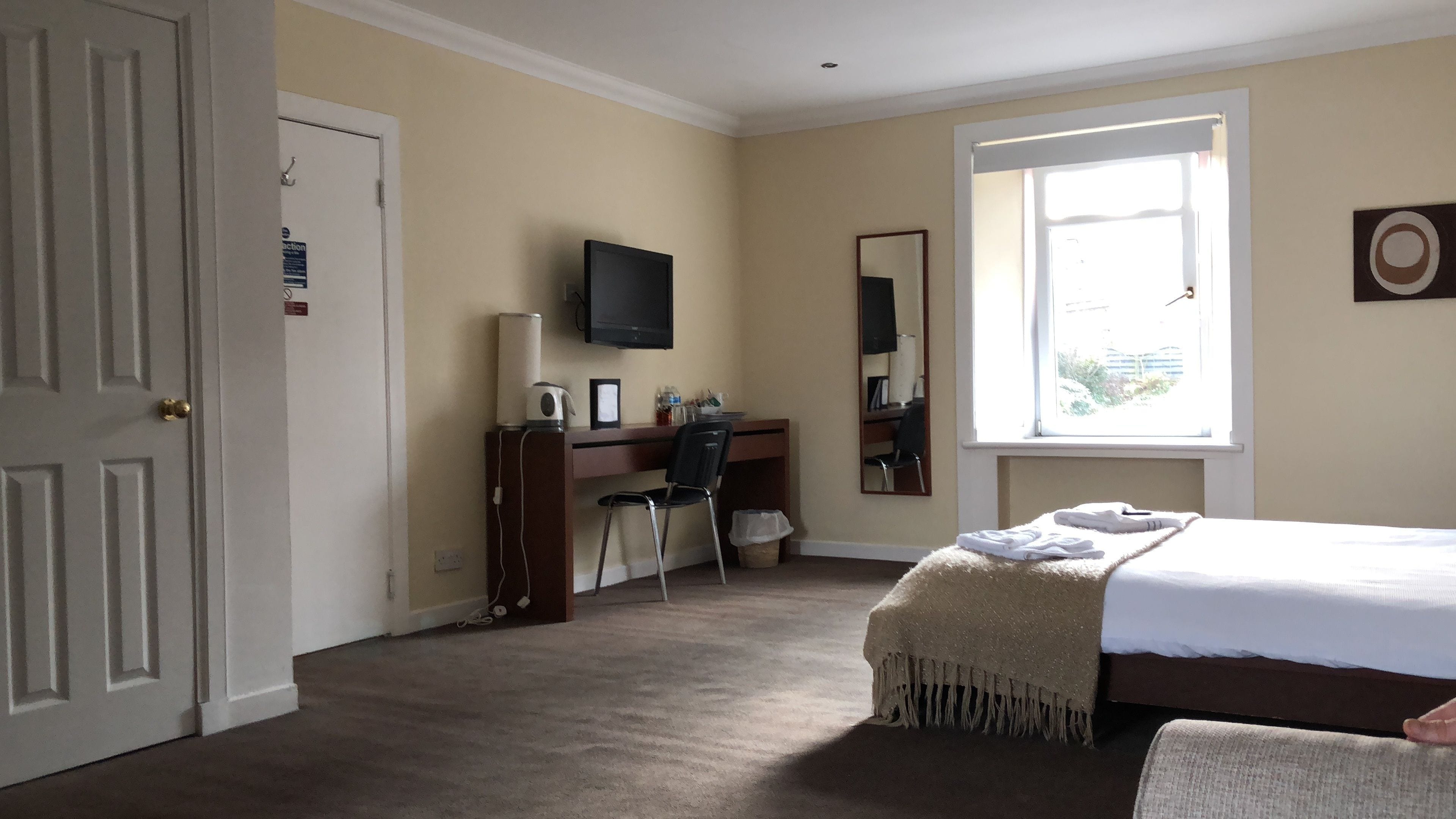 A hotel room with a bed, a desk, a chair, a TV, and a window.