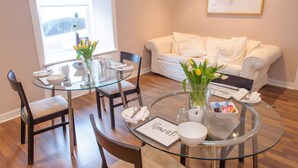 A modern dining area with a glass table, chairs, and a vase of flowers. A white sofa is visible in the background. - Rooms at 31 (Stonehaven)