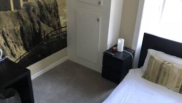 A hotel room with a bed, a nightstand, a desk, a wardrobe, and a mural on the wall.