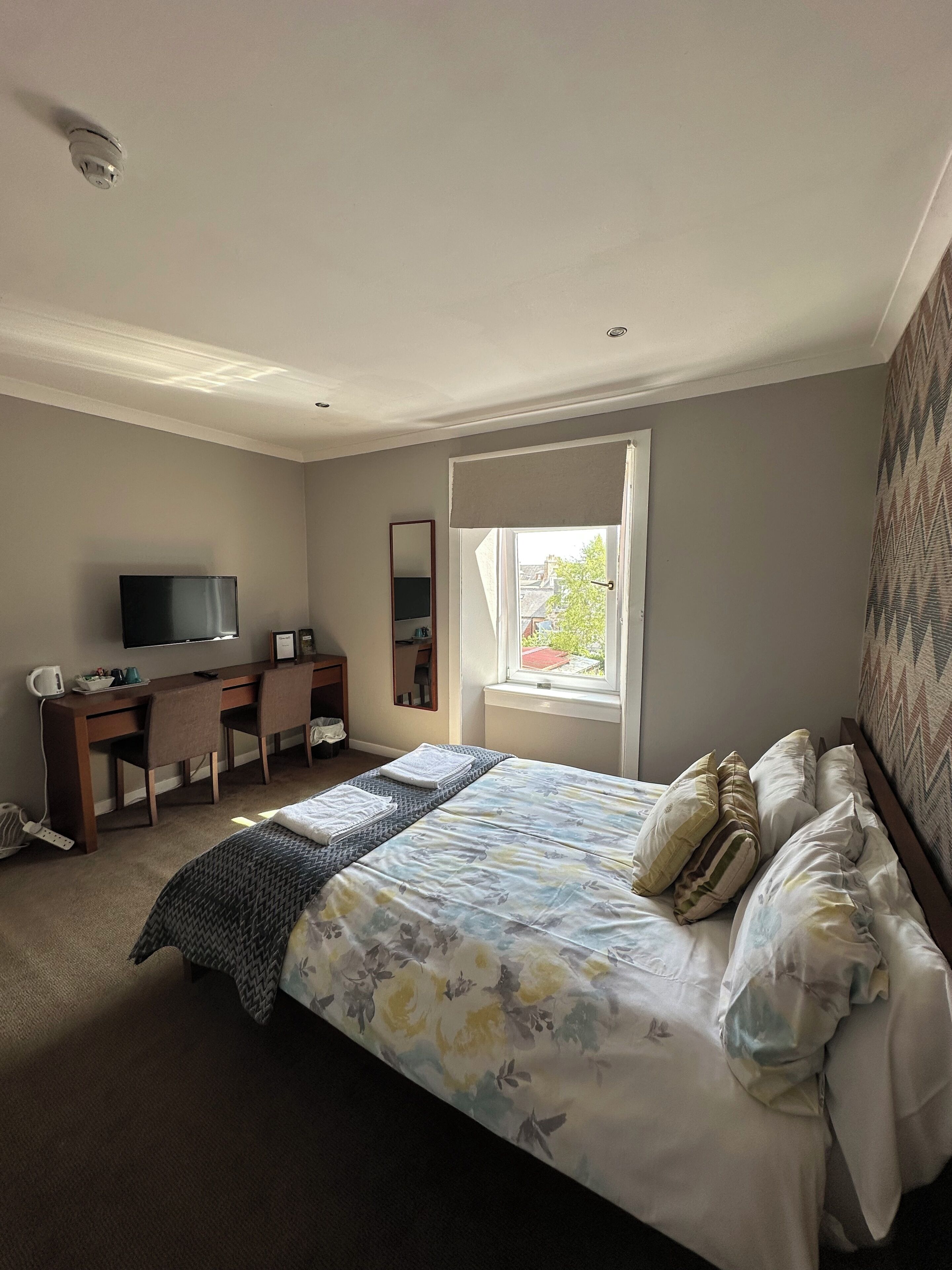 A bedroom with a bed, a desk, a chair, a television, and a window.