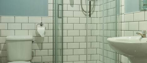 Un baño con ducha envuelta en vidrio, inodoro y lavamanos.