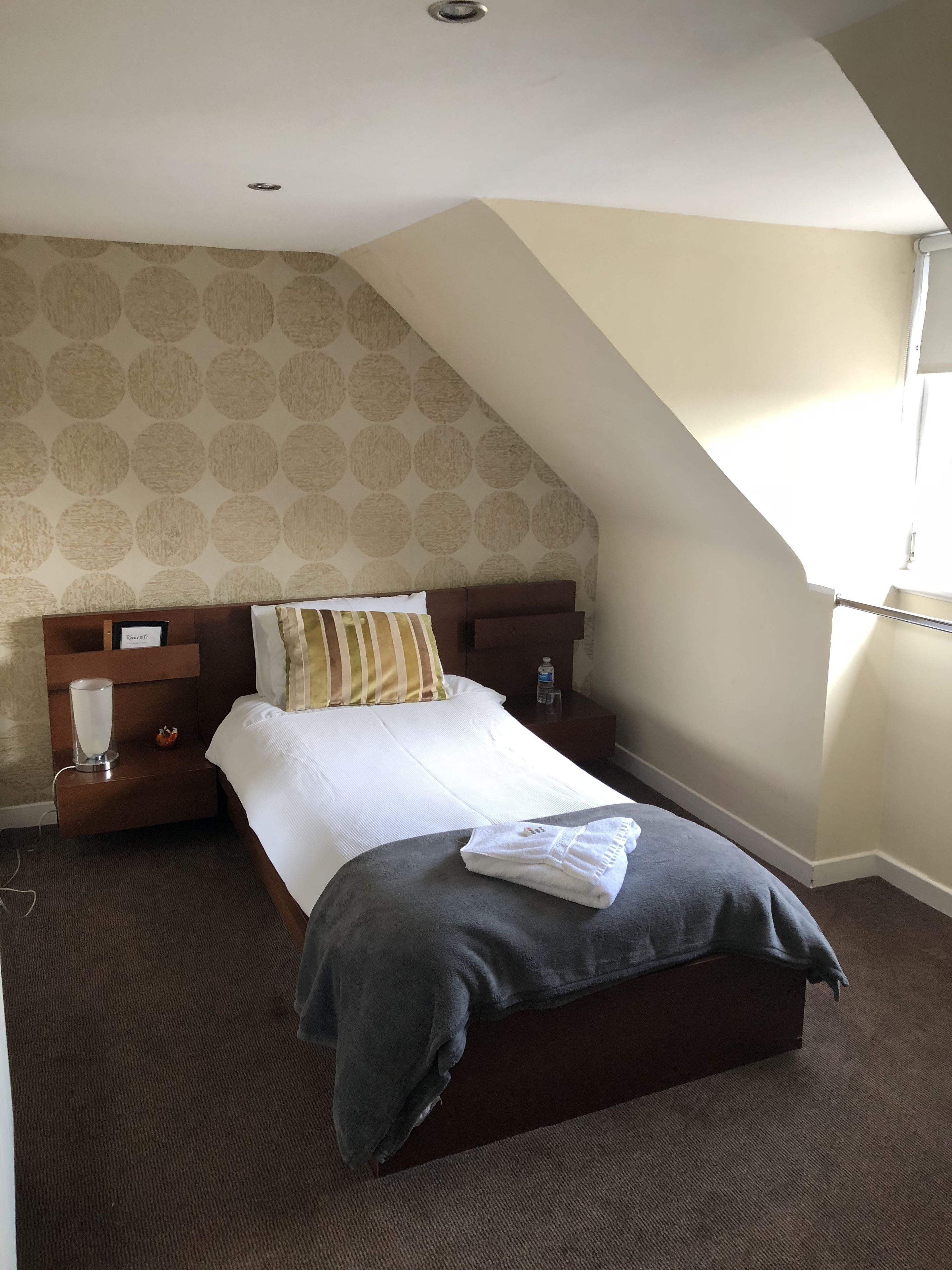 A bedroom with a bed, a nightstand, a lamp, a water bottle, and a towel on the bed.
