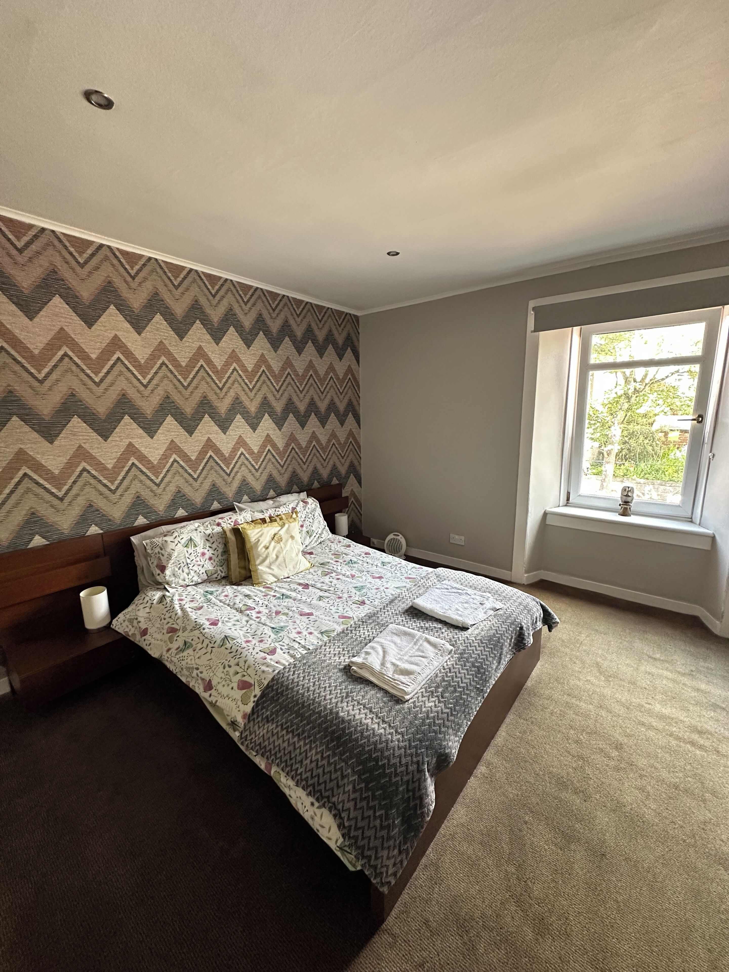 A bedroom with a bed, a bedside table, a window, and a chevron-patterned wall.