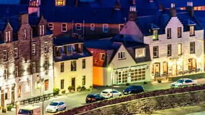 A hotel with multiple stories, a well-lit entrance, and a parking area with several cars. - Rooms at 31 (Stonehaven)