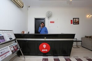 A reception desk with a logo, a fan, and a door in the background. - OYO 11337 Asian Hospitality (Gurugram)