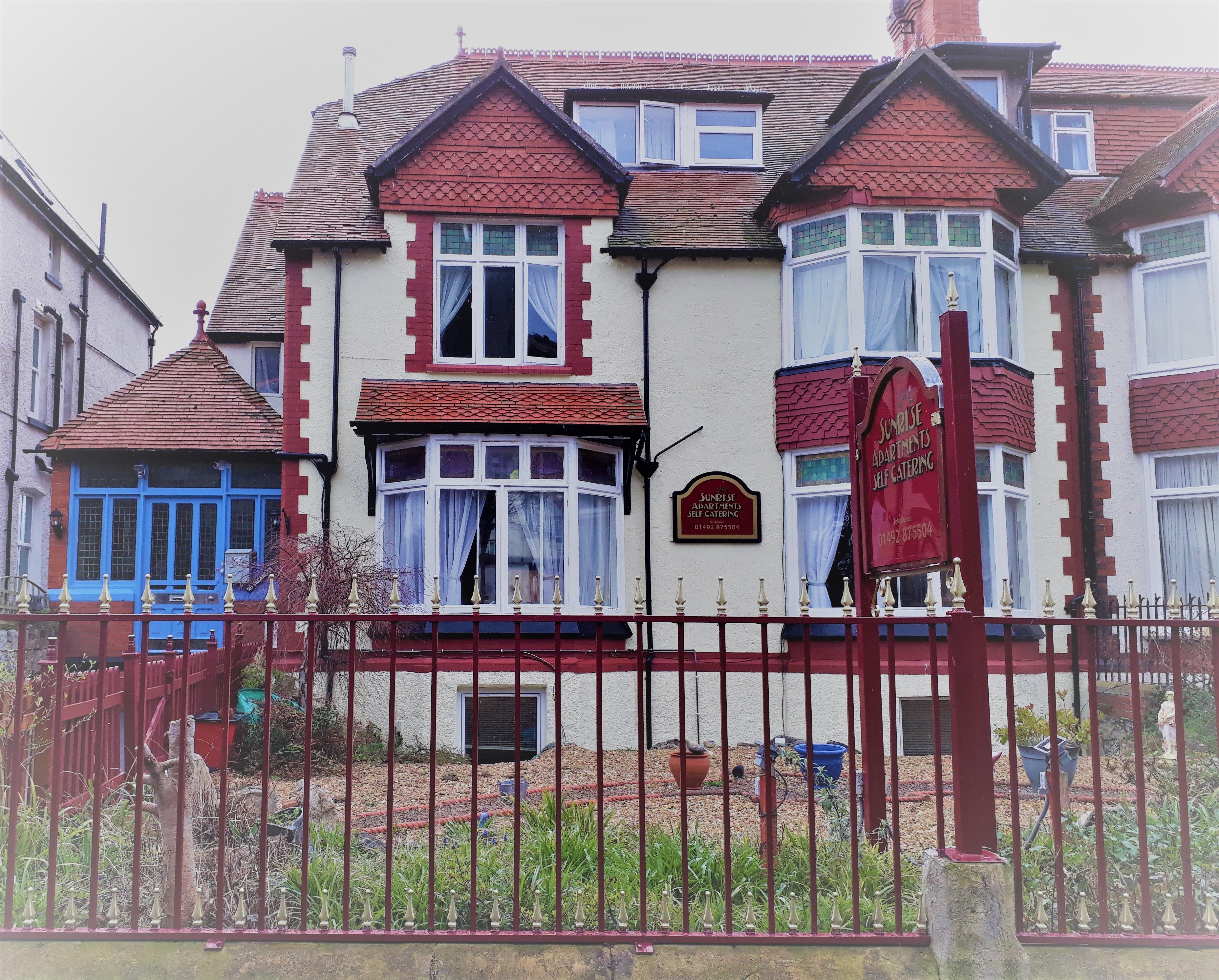 A two-story building with a red and white facade, multiple windows, and a gated entrance.