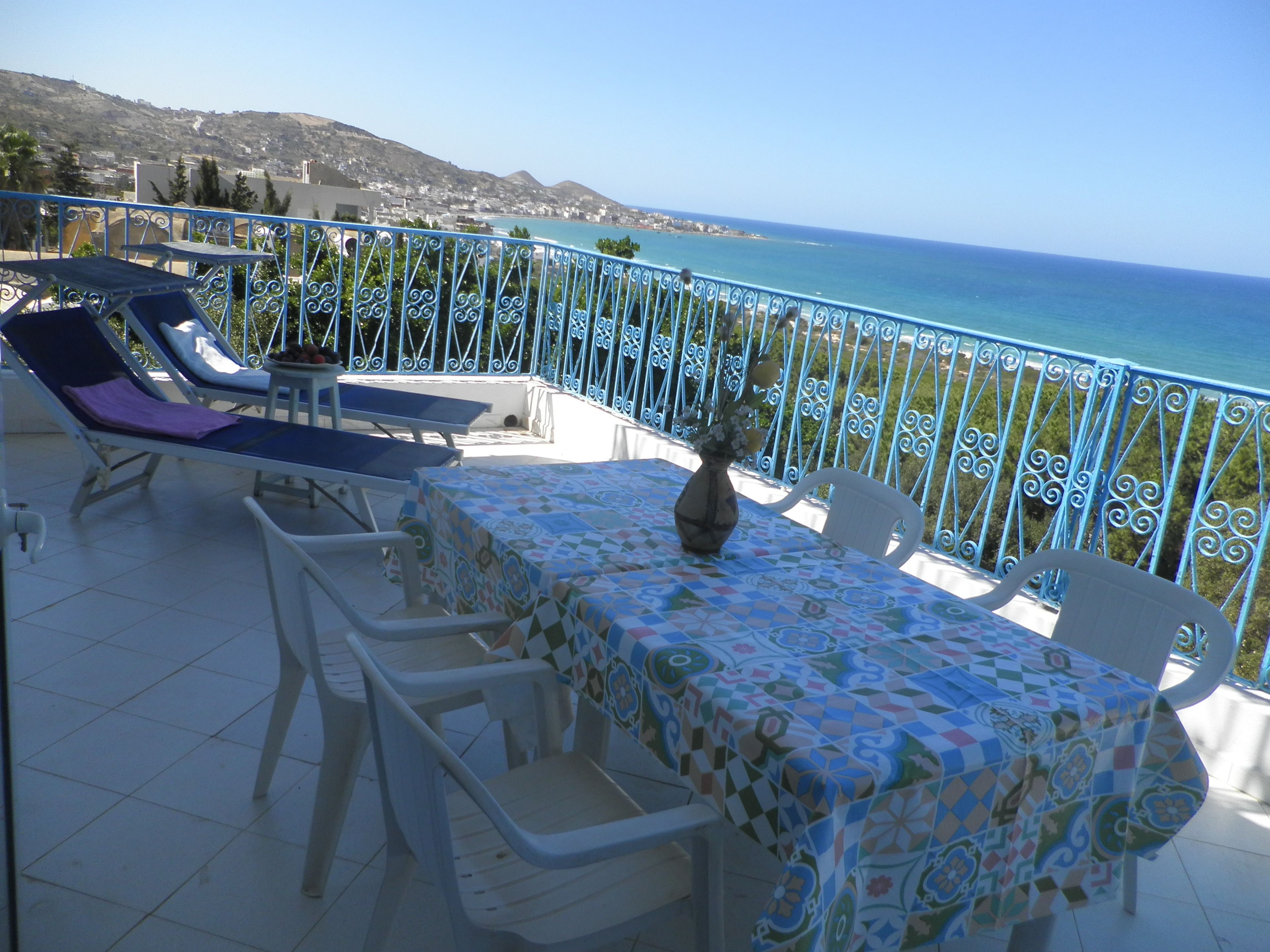A terrace with a table and chairs, overlooking a coastal view.