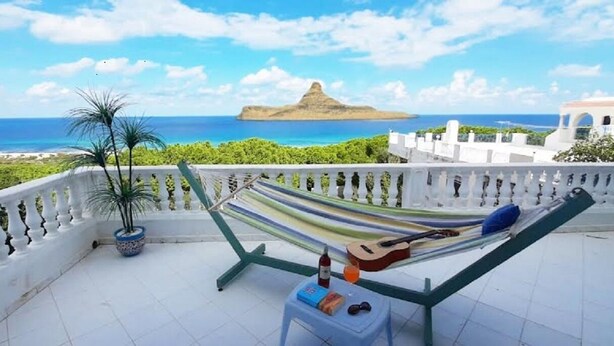 A balcony with a hammock, a potted plant, and a table with a bottle and glasses. - Dar Tomoko & Salah (Raf Raf)