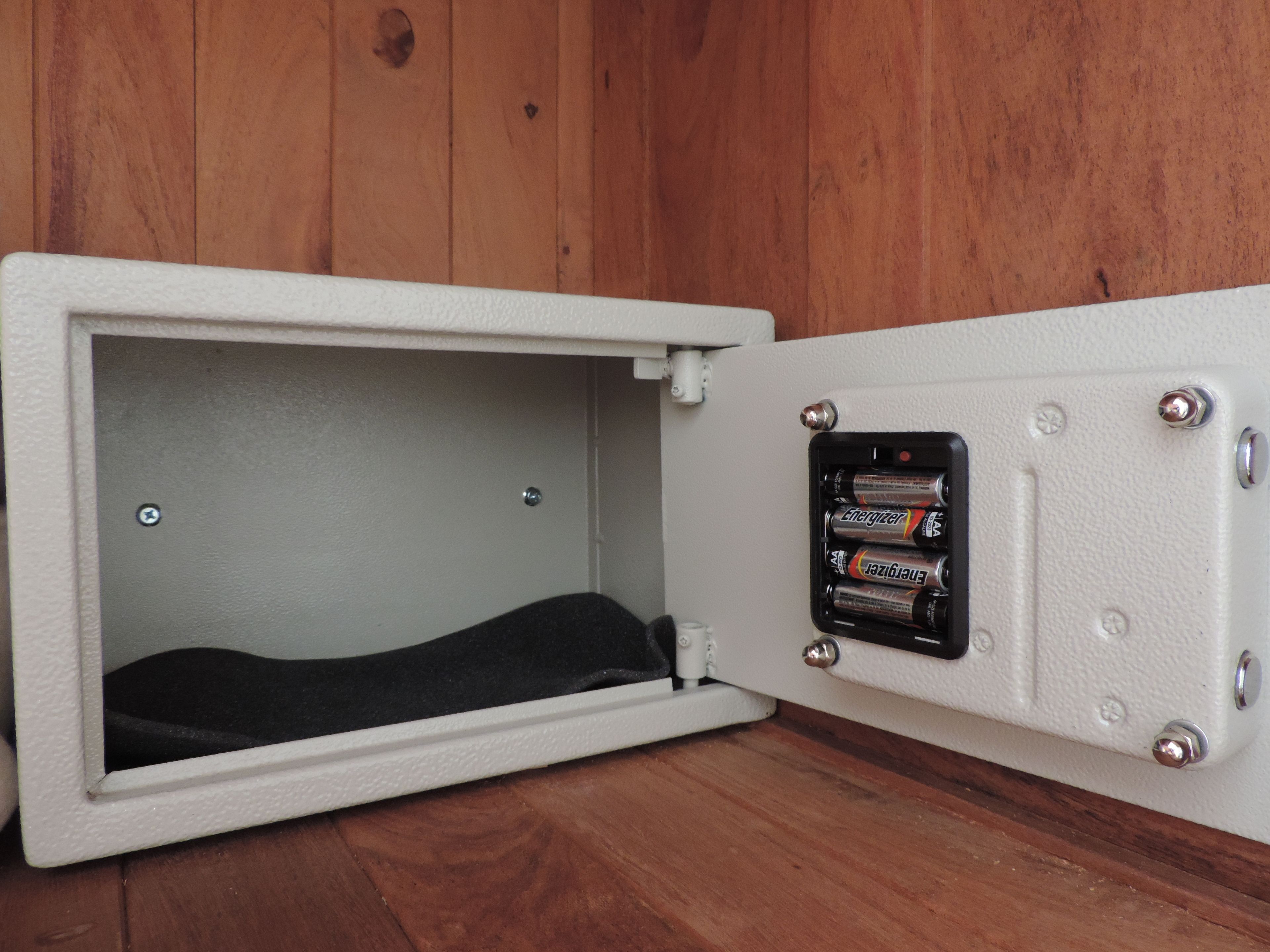 Una caja fuerte blanca con interior negro, fijada a una pared de madera.