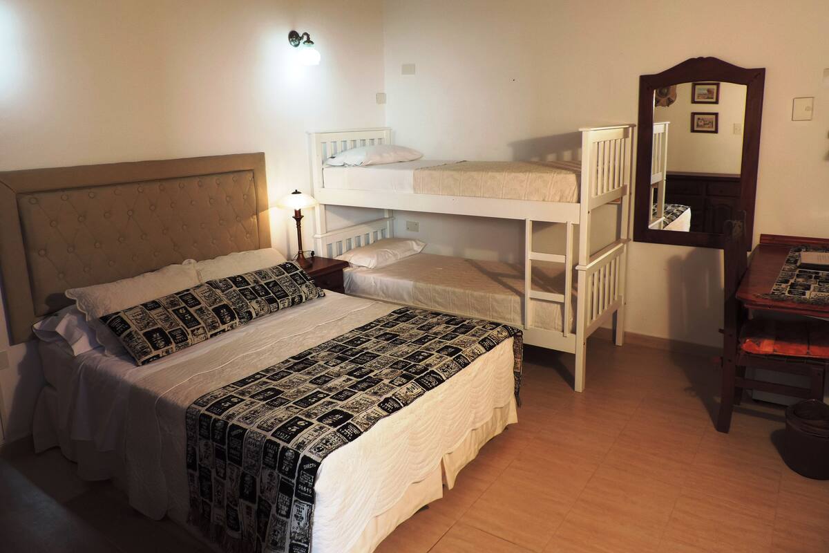 Une chambre avec un lit simple, un lit superposé, une commode en bois et un miroir.