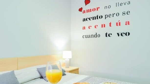 A hotel room with a bed, a breakfast table with croissants, a glass of orange juice, a red rose, and a wall with a love quote. - Hotel Viñas 17 (Teruel)