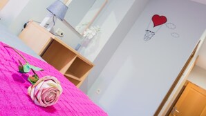 A bedroom with a pink bedspread, a single rose, a bedside table with a lamp, and a wall with a heart and hot air balloon decal. - Hotel Viñas 17 (Teruel)