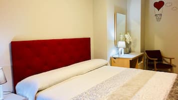 Hotelkamer met een rode hoofdbord, een bed met beddengoed met een patroon, een bureau met lamp, een stoel en een wanddecoratie van een hart en wolken.