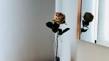 A single rose in a clear vase on a wooden table next to a mirror.