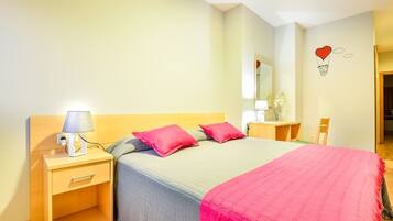 A bedroom with a bed, a nightstand, a lamp, a mirror, and a wall decoration.