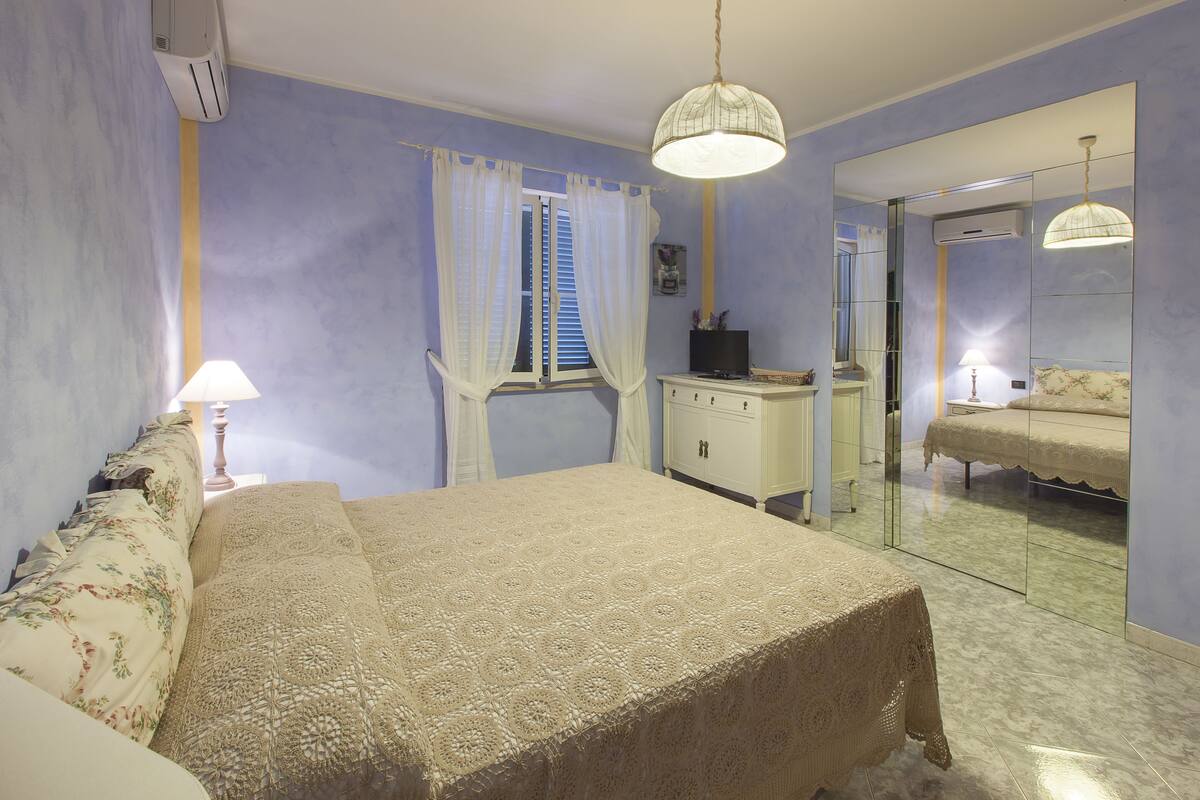 A bedroom with a bed, a dresser, a mirror, and a window with curtains.