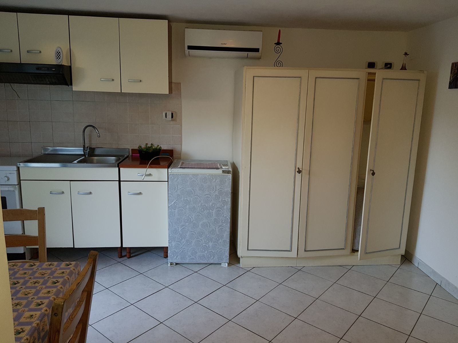 Cocina compacta con lavamanos, estufa y armarios. Incluye un refrigerador pequeño y una mesa de comedor con sillas.