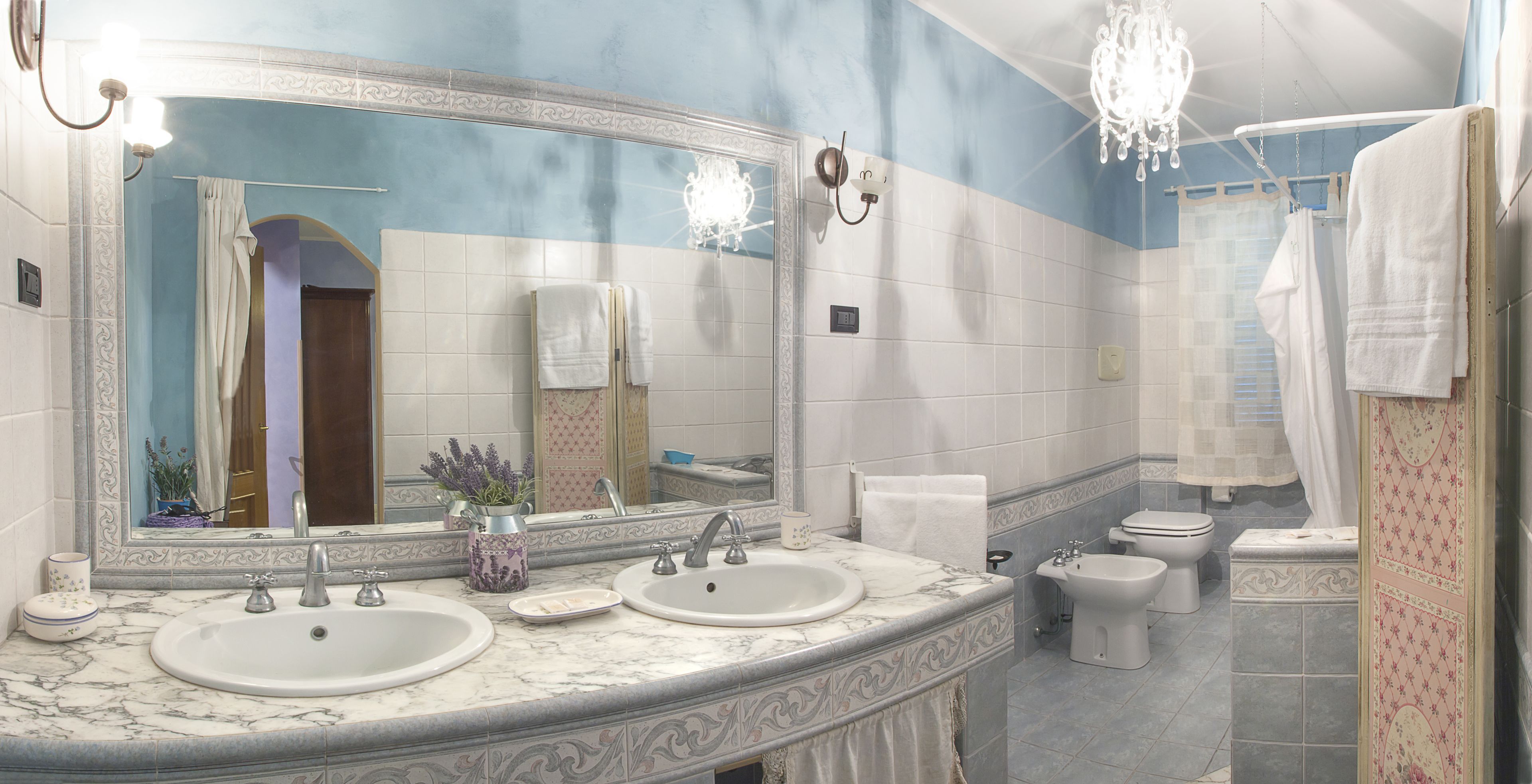 A bathroom with two sinks, a large mirror, a chandelier, and a toilet.
