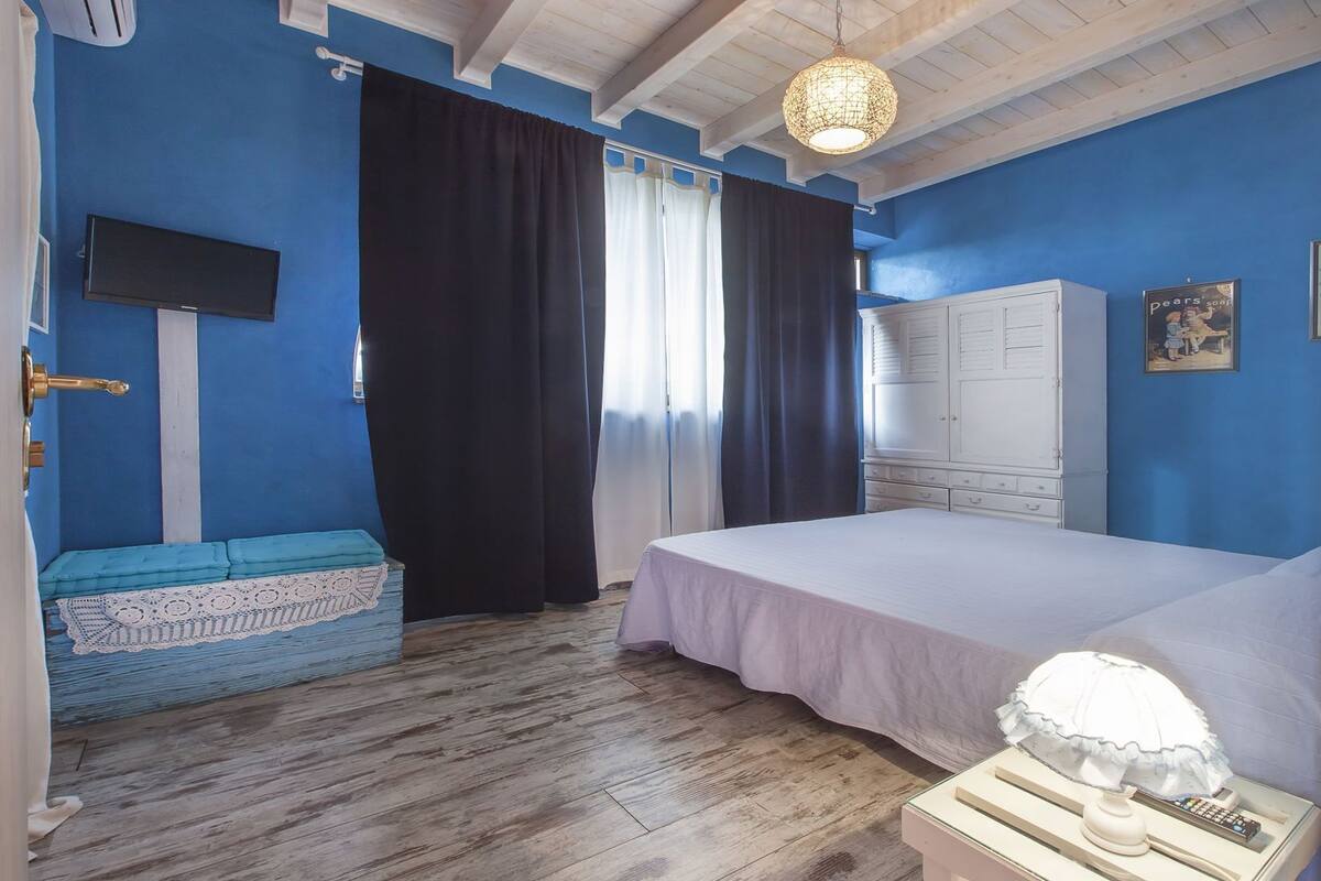A bedroom with a bed, a wardrobe, a TV, and a window with curtains.