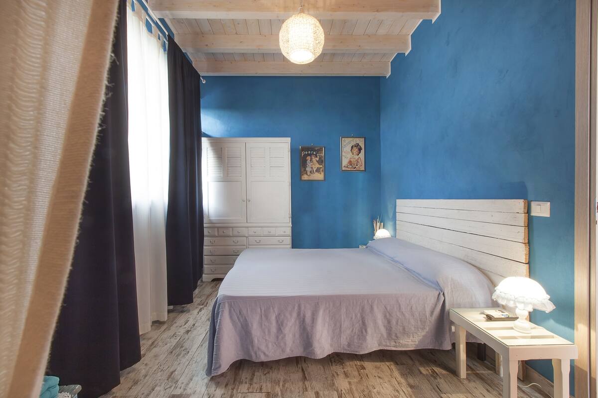 A bedroom with a bed, a nightstand, a lamp, and a wall with two pictures.