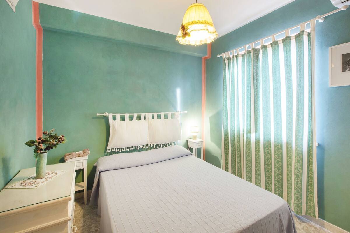 A bedroom with a bed, bedside table, lamp, and curtains.
