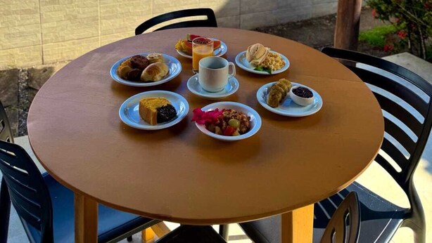 A table with breakfast items and a view of a swimming pool. - Pousada Coral de Fogo (Prado)
