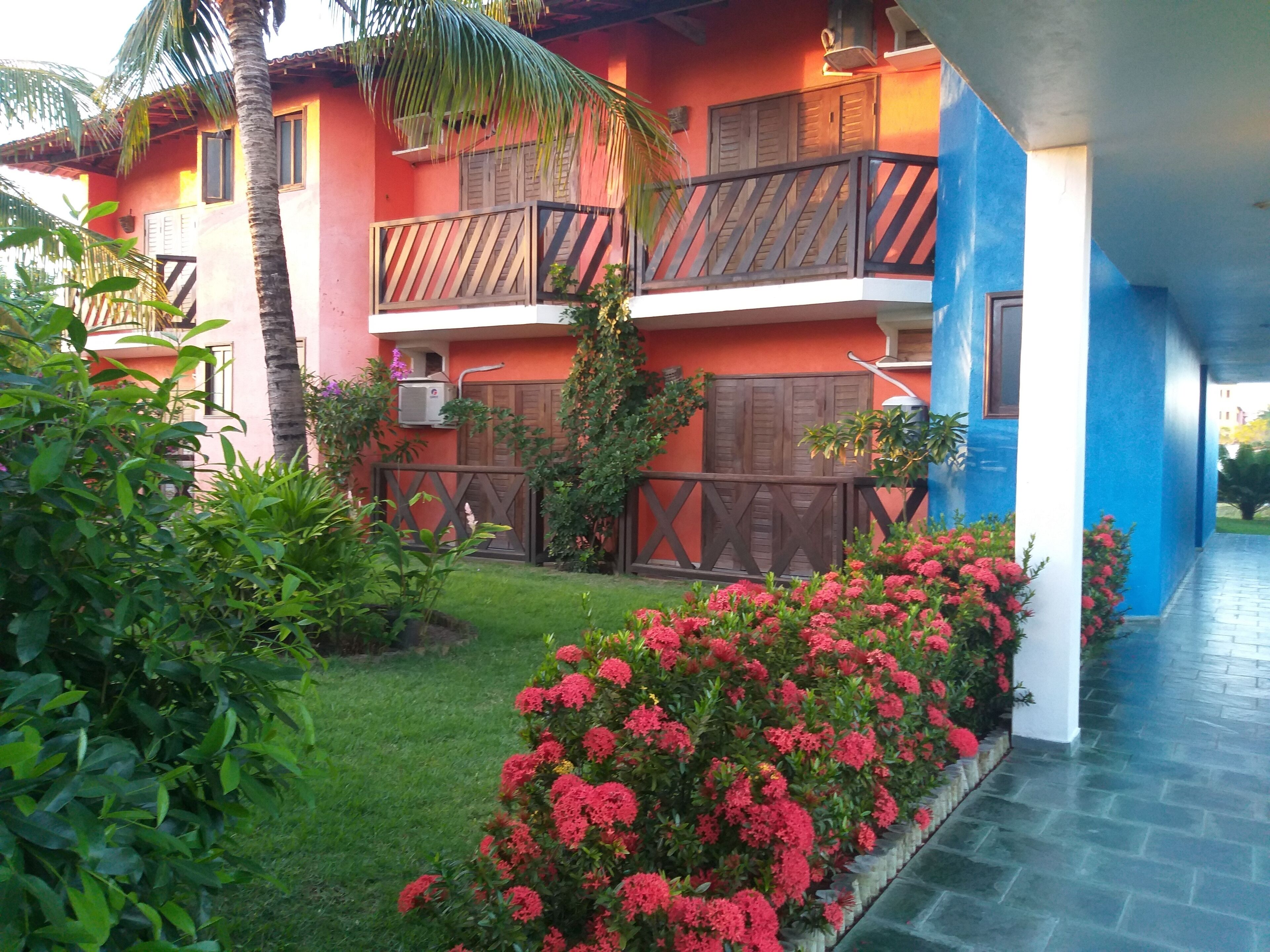 Ein zweistöckiges Gebäude mit Balkon, umgeben von üppigem Grün und farbenprächtigen Blumen.