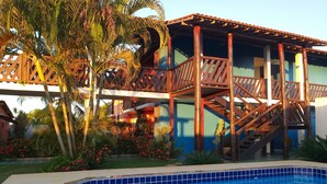 A pool area with a wooden deck and stairs leading to a building with balconies. - Pousada Coral de Fogo (Prado)