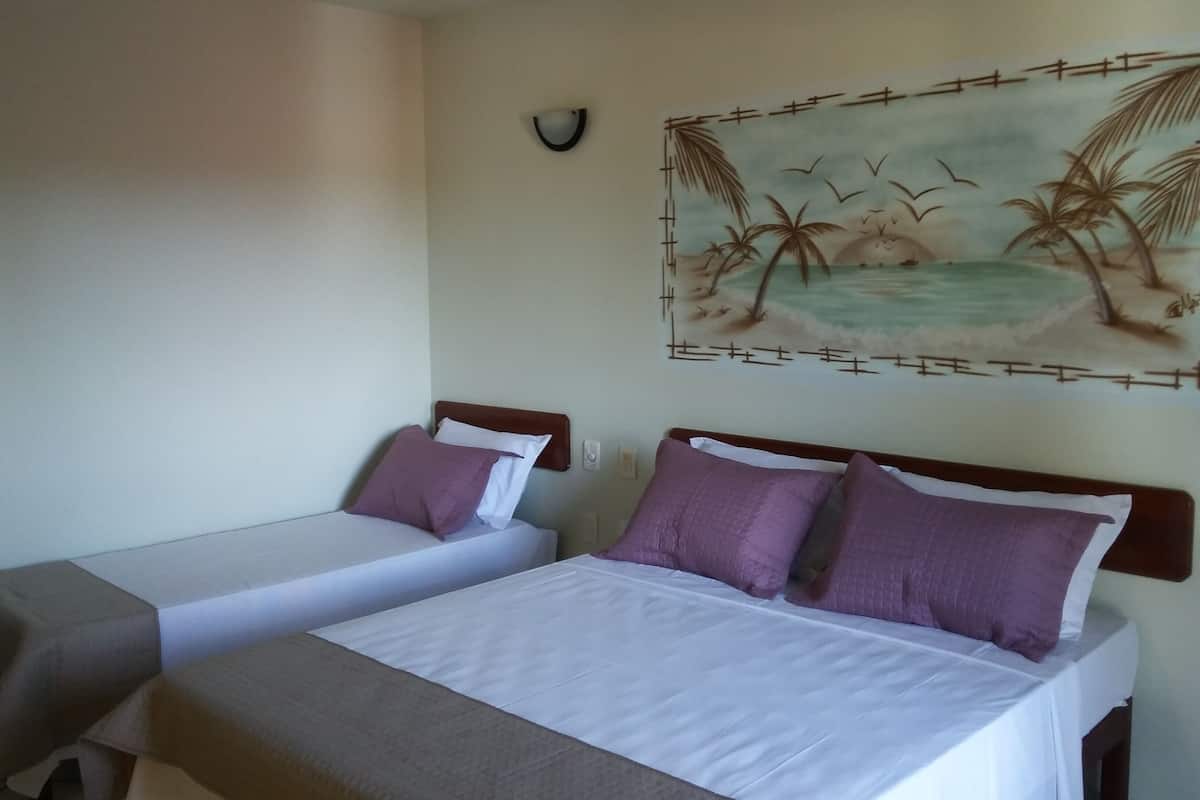 A hotel room with two single beds, each with a wooden headboard, white bedding, and purple pillows.