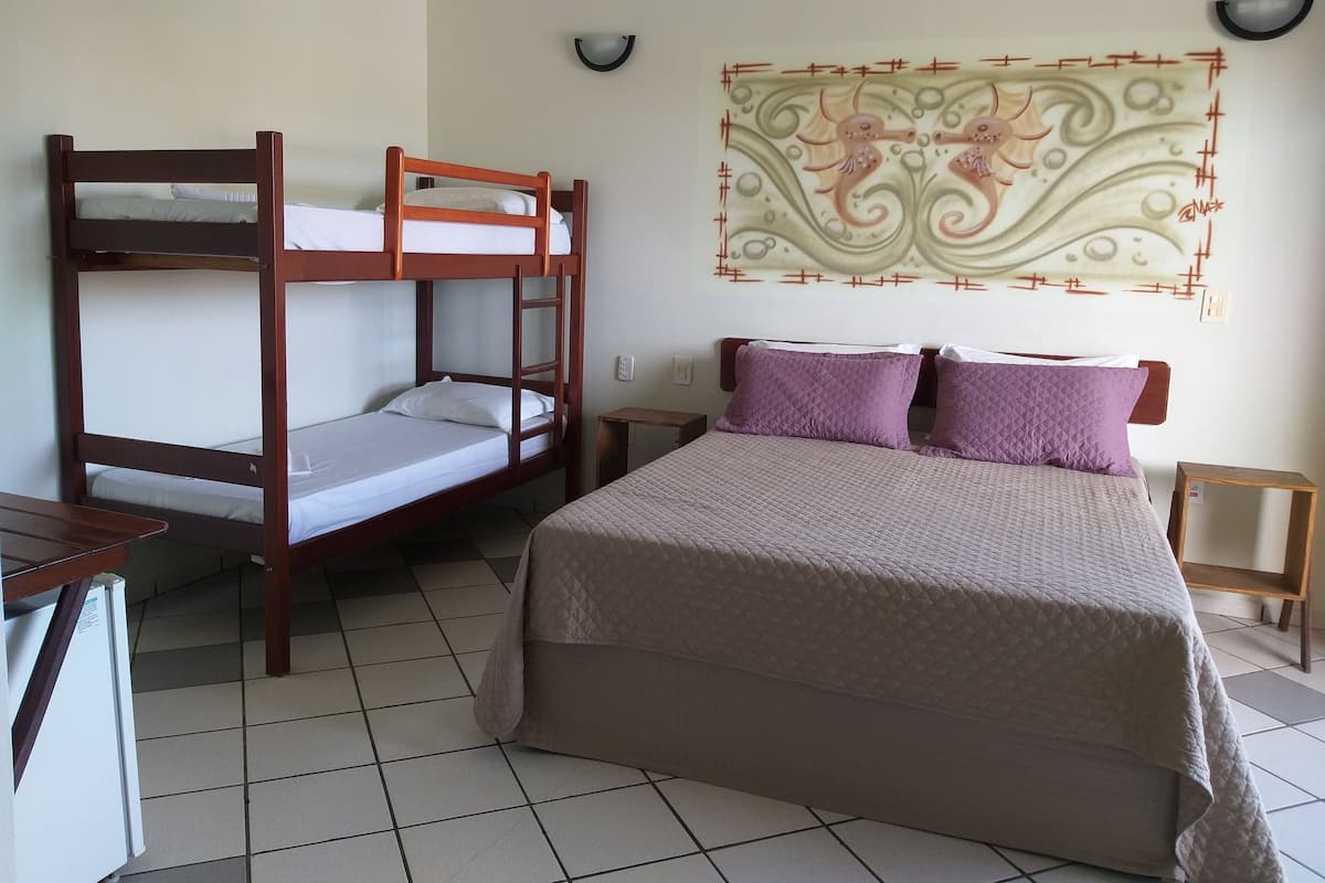 A room with a bunk bed, a single bed with a quilted bedspread, and a wall-mounted light fixture.