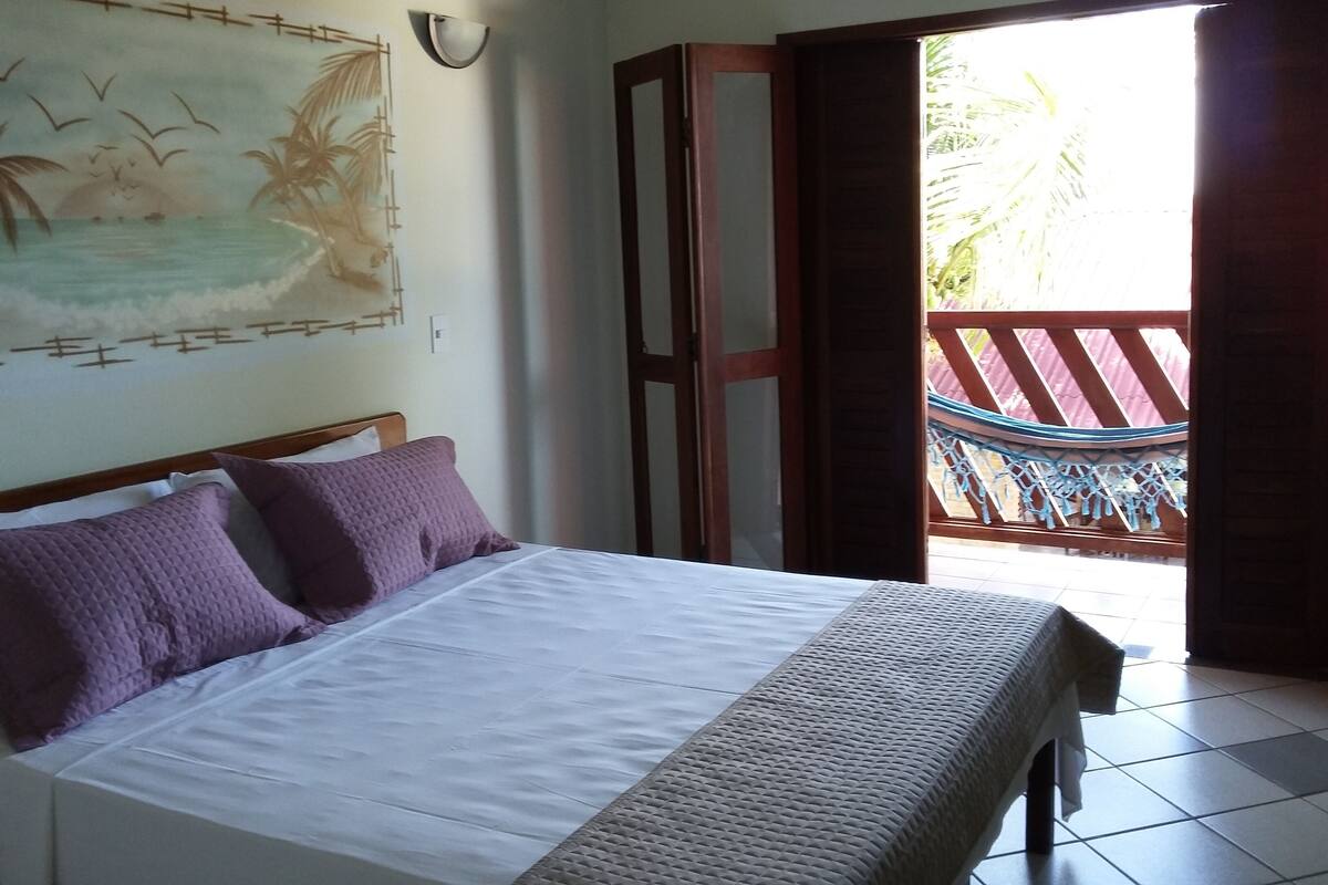 A bedroom with a bed, a wall-mounted artwork, a door leading to a balcony, and a hammock.