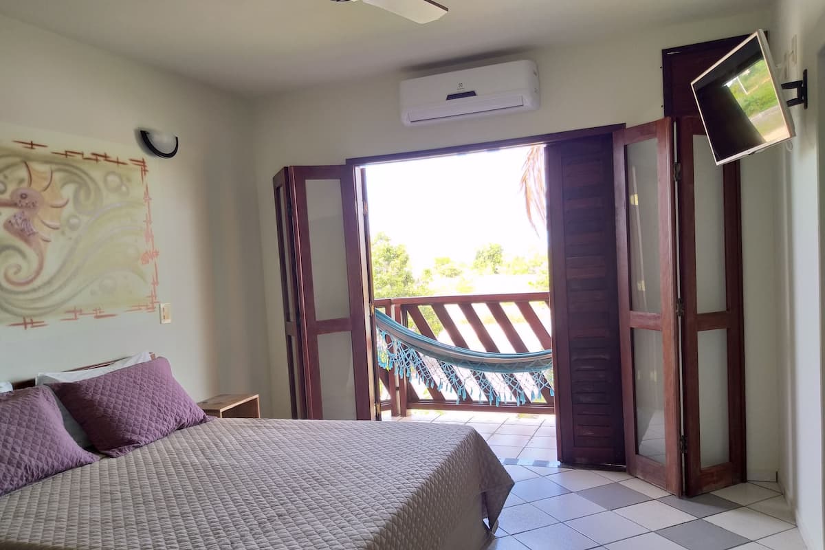 A bedroom with a bed, a TV, an air conditioning unit, and a view of the outside.