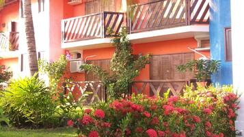 A two-story building with balconies, a garden with red flowers, and a palm tree.