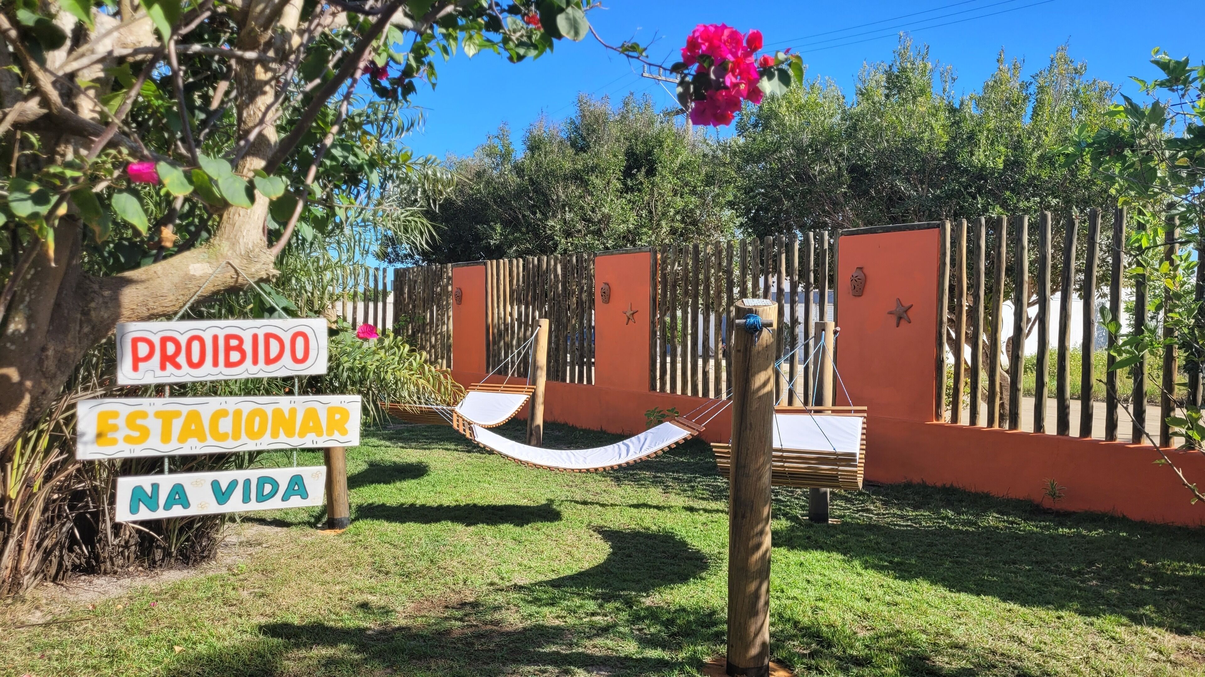 Un espace délimité par une clôture, avec un hamac et des panneaux en portugais.