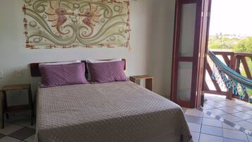 A bed with a quilted cover, two nightstands, a wall-mounted decorative piece, and a view of a balcony with a hammock.