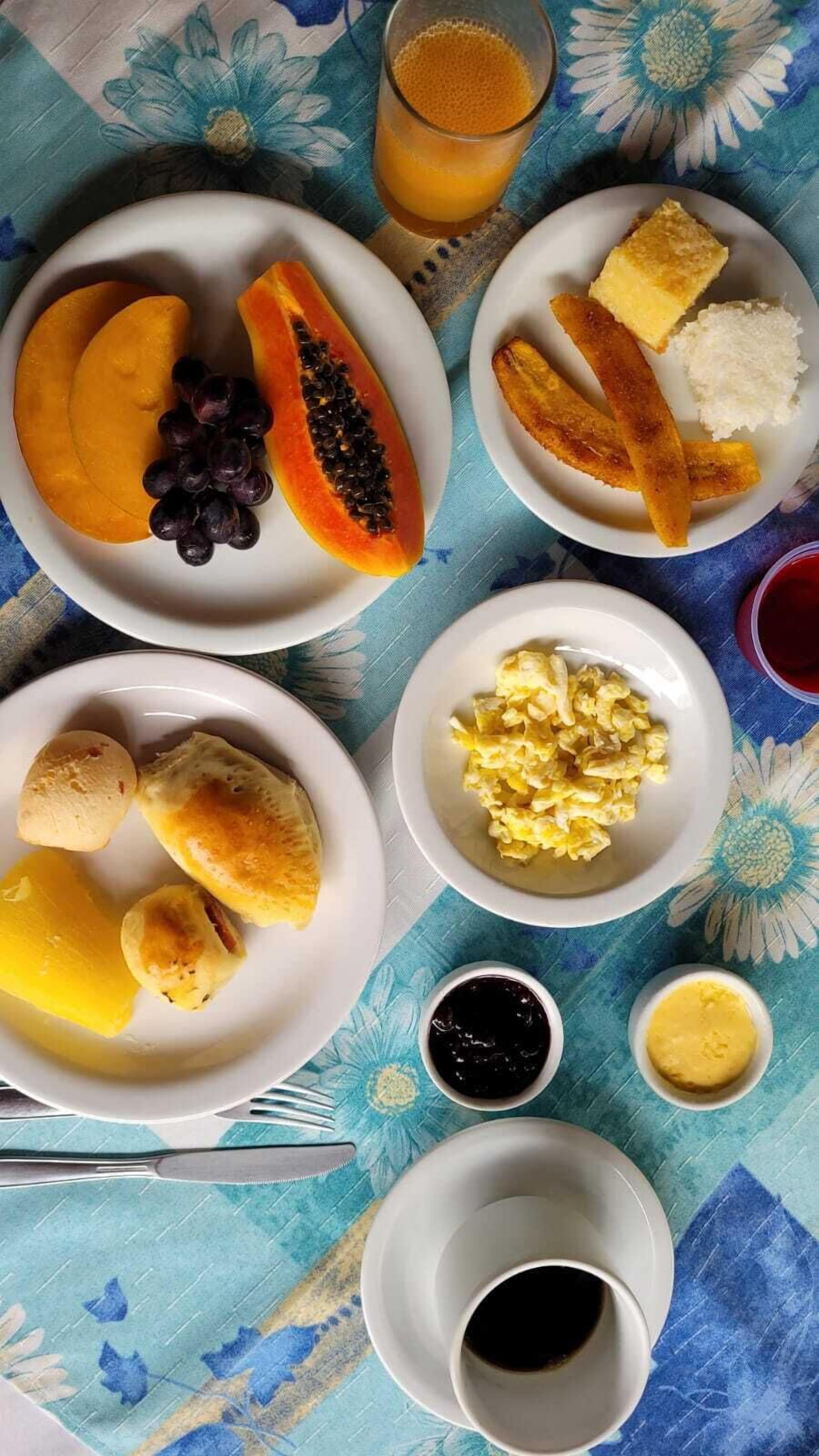 Een tafel met borden eten, waaronder fruit, eieren en rijst. Ook staan daar bekers koffie en sap.