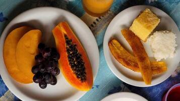 Een tafel met borden eten, waaronder fruit, eieren en rijst. Ook staan daar bekers koffie en sap.