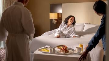 A hotel room with a neatly made bed, a bedside table with breakfast items, and a nightstand with a lamp.